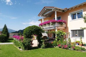 A two-story house with a balcony adorned with flowers, a well-maintained garden, and a mountain in the background. - Holiday apartment in Grän with swimming pool (Grän)