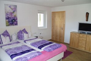 Ein Schlafzimmer mit zwei Betten, einem Fernseher, einem Holzschrank, einem Fenster und einer Tür.