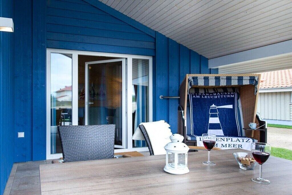 Een blauw gebouw met een overdekt terras, een tafel met twee glazen rode wijn, en een bord met een afbeelding van een vuurtoren.