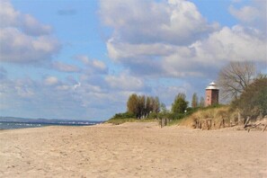 A sandy beach with a lighthouse and trees in the background.