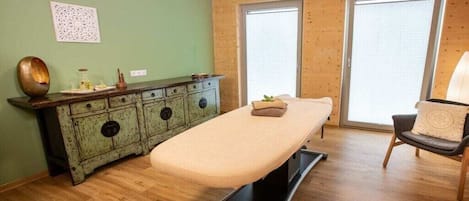Una habitación con una camilla de masaje, un armario de madera y una silla.
