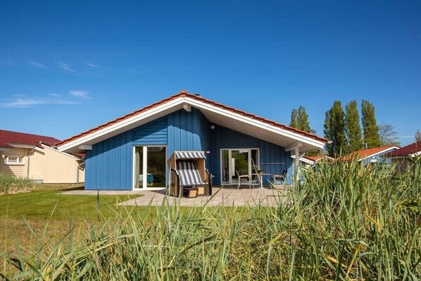 A blue house with a red roof, a patio with a table and chairs, and a grassy area in front.