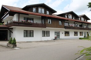 A two-story hotel with a white facade, balconies with flower boxes, and a parking lot in front. - Holiday apartment with 2 bedrooms (Oberstaufen)