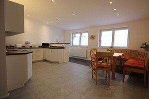 A kitchen with white cabinets, a dining table with chairs, and a window with blinds. - Holiday apartment with 2 bedrooms (Oberstaufen)