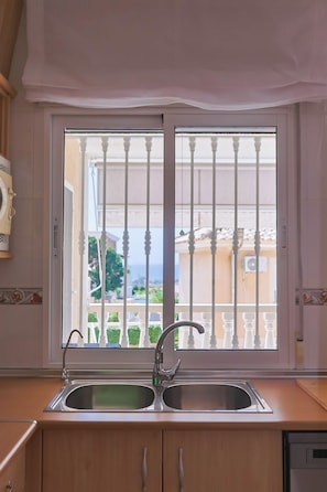 A kitchen with a double sink, a window with a white balustrade, and a view of the sea.
