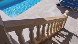 Ein Schwimmbecken mit gefliestem Deck, einem weißen Geländer und einem blauen Sonnenschirm.