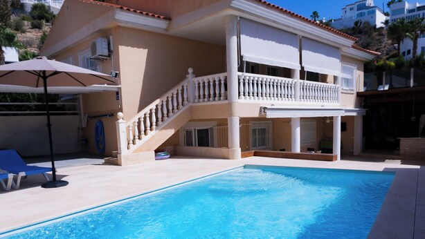 Ein zweigeschossiges Gebäude mit Swimmingpool, überdachter Terrasse und einer Treppe, die zum oberen Stockwerk führt.