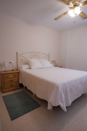 A bedroom with a bed, a nightstand, a dresser, a ceiling fan, and a rug.