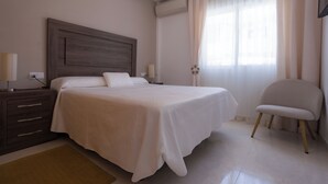 Ein Schlafzimmer mit einem Bett, Nachttischen, einem Sessel und einem Fenster mit Vorhängen.