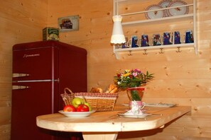 Ein Holzinnenraum mit einem roten Gerät, einem Tisch mit Früchten, einem Korb und einer Vase mit Blumen.
