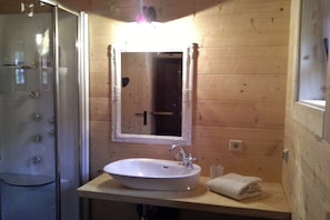 Ein Badezimmer mit Duschkabine aus Glas, einem weißen Waschbecken mit Spiegel darüber und Holzwänden.