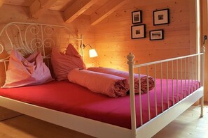 Ein Einzelbett mit weißem Metallgestell, roter Bettwäsche und einem Kopfteil mit einer Leuchte.