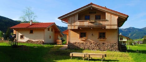 A two-story wooden house with a red roof, a balcony on the upper floor, and a stone foundation.