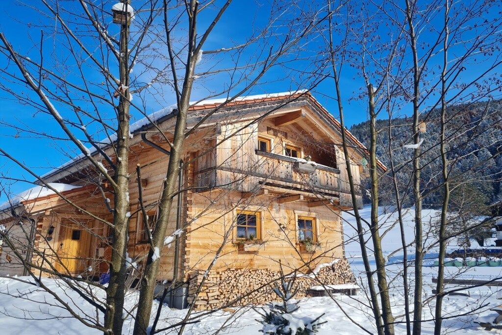 A wooden chalet with a balcony, surrounded by snow-covered trees.