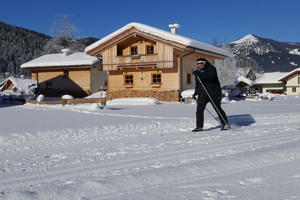 A wooden chalet with a balcony, surrounded by snow-covered houses and mountains.