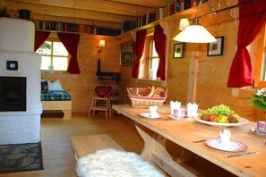 Ein gemütliches Blockhaus-Interieur mit Kamin, Holzwänden, einem Esstisch mit Obst und einem Korb sowie einer Bank.