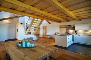 Eine geräumige Küche mit weißen Schränken, einer Holztruhe und einer Treppe, die in eine obere Ebene führt.