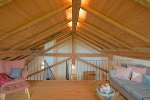 Een kamer onder het dak met een schuine houten plafond, een trap, een bank, een stoel en een kleine tafel met kaarsen.