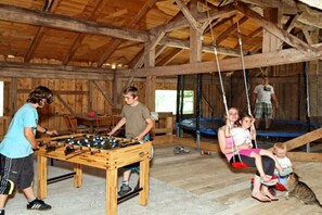 A rustic wooden interior with a foosball table, a trampoline, and a swing set. - Forest view from the Pletl farm (Schönberg)