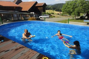 Una piscina con bordo in legno, circondata da case e un cielo sereno.