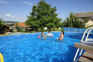 En swimmingpool med kristallklart blått vatten, omgiven av träd och ett trädäck.