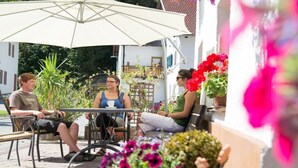 Ein Sitzbereich im Freien mit Tischen und Stühlen, umgeben von Blumentöpfen und Blumen.
