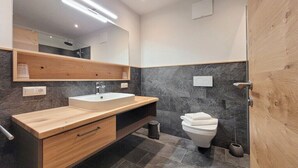 Ein modernes Badezimmer mit einem Holzbidet, einem weißen Waschbecken, einer Toilette und einem großen Spiegel.