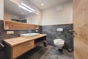Een moderne badkamer met een houten wastafelmeubel, een witte wasbak, een toilet en een grote spiegel.
