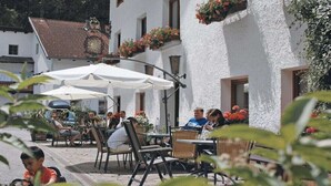 Ein Straßencafé mit Tischen und Stühlen, umgeben von weißen Gebäuden mit Blumenkästen.