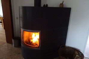 A wood-burning stove with a visible fire, a basket to the right, and a door frame to the left. - Holiday apartment in Sarkwitz with parking (Sarkwitz)