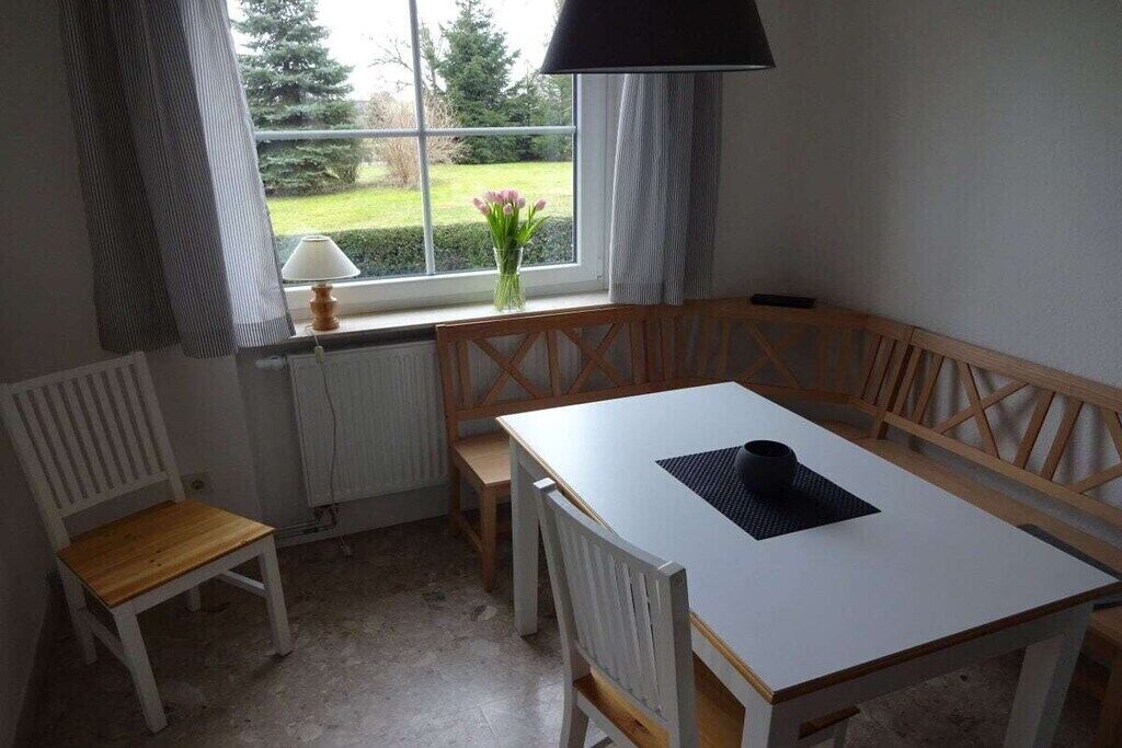 Ein Zimmer mit einem weißen Tisch, einer hölzernen Bank und einem Fenster mit Blick auf Grünflächen.