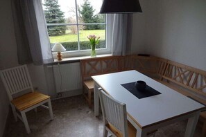 A room with a white table, wooden bench, and a window with a view of greenery. - Holiday apartment in Sarkwitz with parking (Sarkwitz)