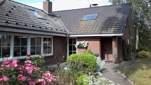 Una casa a due piani con tetto spiovente, un camino e un piccolo giardino fiorito.