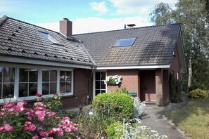 A two-story house with a sloped roof, a chimney, and a small garden with flowers. - Holiday apartment in Sarkwitz with parking (Sarkwitz)