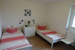 A bedroom with two single beds, a bedside table with a vase of flowers, a small desk, and a chair. - Holiday apartment in Sarkwitz with parking (Sarkwitz)