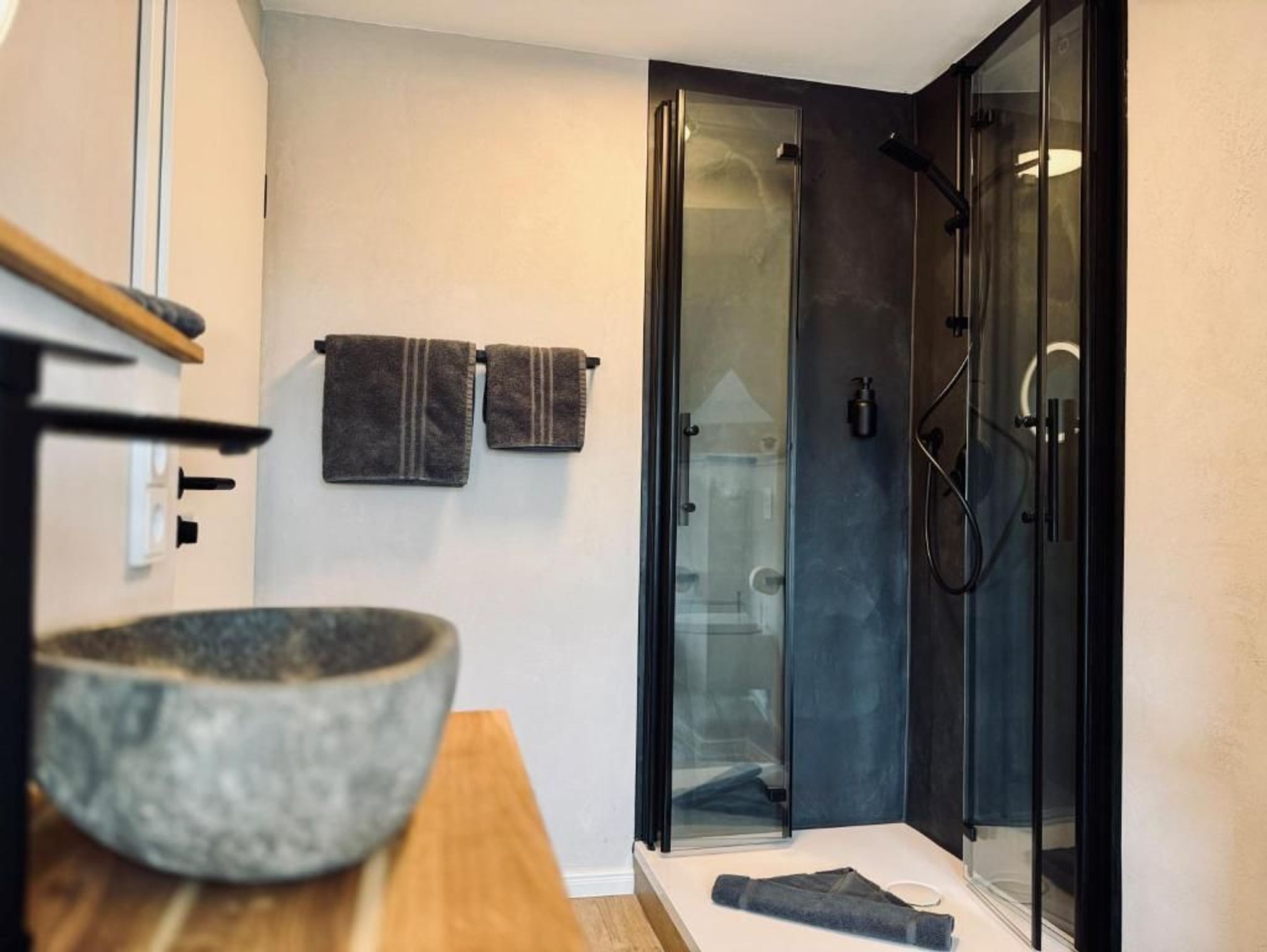 Ein modernes Badezimmer mit einer Duschkabine aus Glas, einer Holztischplatte und zwei Handtüchern, die an der Wand hängen.