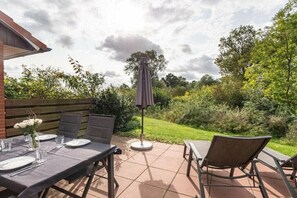 An outdoor patio with a table set for dining, surrounded by chairs and an umbrella. - Holiday Village 39 B (Boltenhagen)
