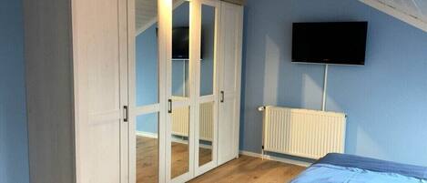 A bedroom with a bed, a wardrobe, a television, and a radiator.