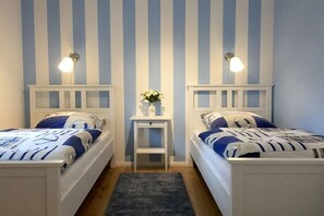 Un dormitorio con dos camas, una mesita con un florero y luces fijadas a la pared.