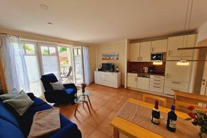 A living room with a sofa, a small table, and a television. There is a kitchen area with cabinets and a microwave. - Holiday apartment in Rerik with swimming pool (Rerik)
