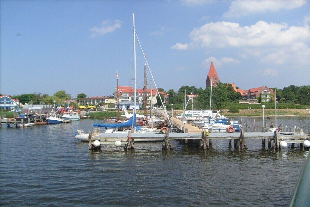 A marina with boats docked, a pier, and buildings in the background.