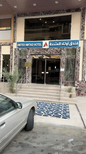 The entrance to the United Awlad Hotel with a marble facade and a car parked in front. - Outad United Hotel 2 (Makkah)