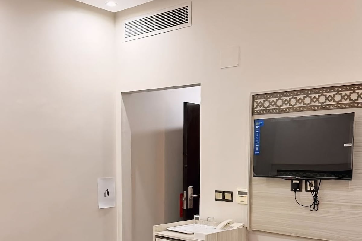 A hotel room with a bed, a desk, a trash bin, a mirror, and a television.