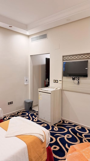 Habitación de hotel con cama, escritorio, cubo de basura, espejo y televisor.