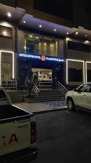 Entrada de un hotel con un cartel que dice United Awtad Hotel, una escalera que lleva a la entrada y un coche estacionado.