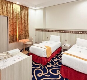 A hotel room with two beds, a desk, a chair, and a bathroom. - Outad United Hotel 2 (Makkah)