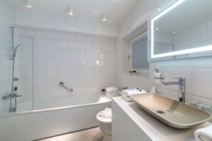 Ein modernes Badezimmer mit einer gläsernen Duschkabine, einer freistehenden Badewanne, einem Waschtisch mit Beige-Becken und einem großen Spiegel.