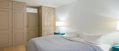 Un dormitorio con cama, mesitas de noche, lámpara y armario.