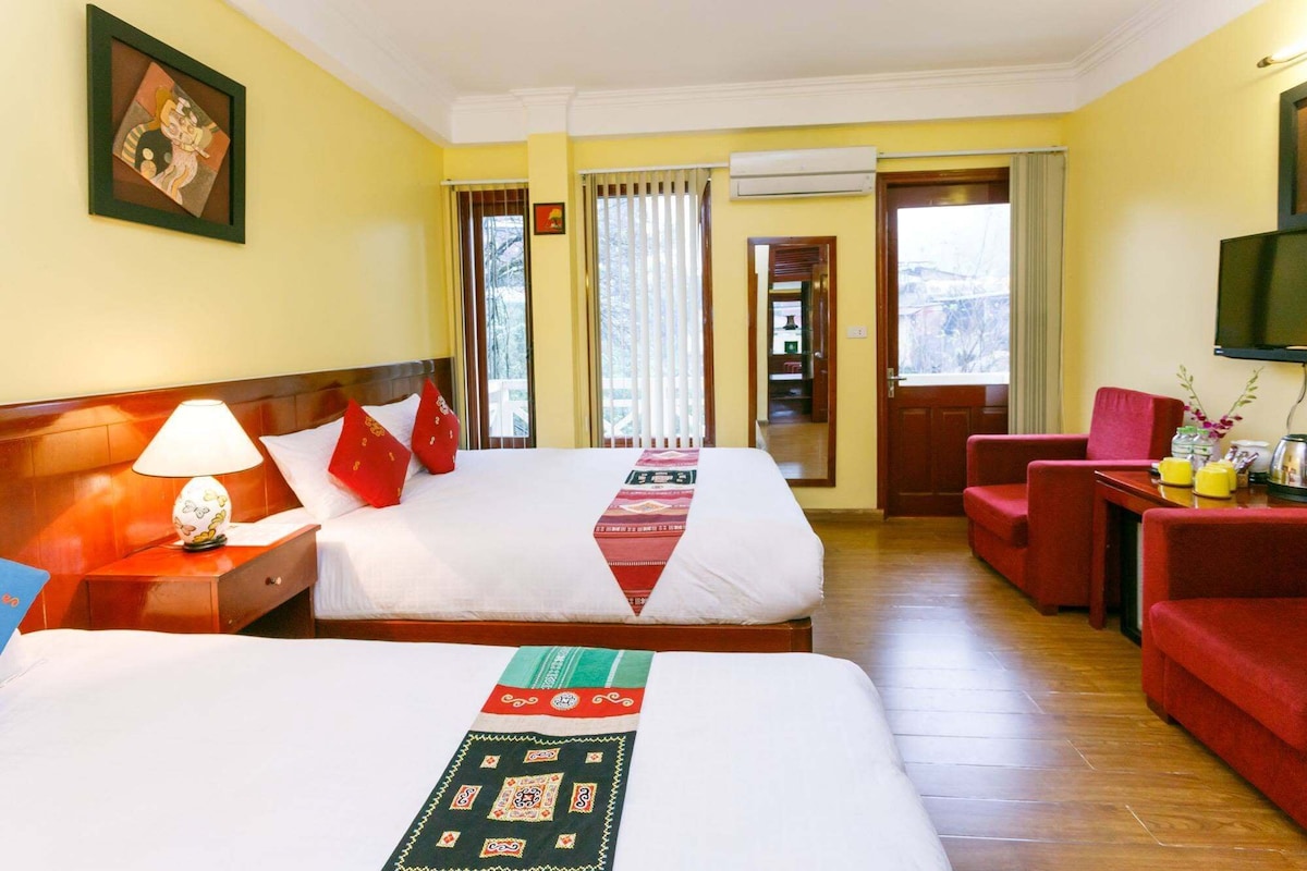 A hotel room with two beds, a sitting area with a red sofa, a television, and a window with curtains.