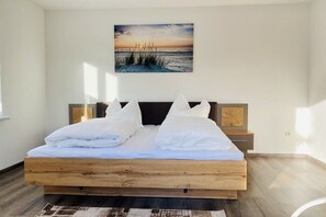 A bedroom with a wooden bed, white bedding, and a beach sunset painting on the wall. - Holiday apartment in Walow with swimming pool (Walow)